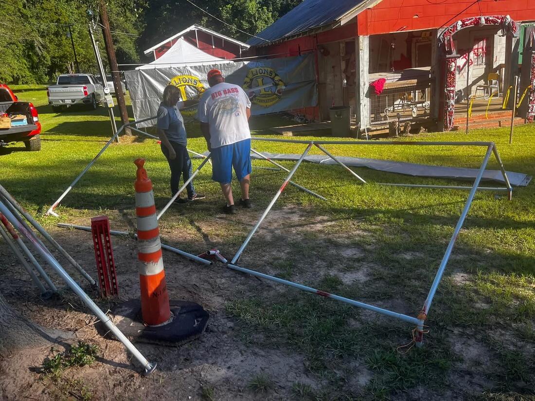 Two Hemphill Lions Club members assembling a tent frame together, Lions International banners hung on the fence behind them